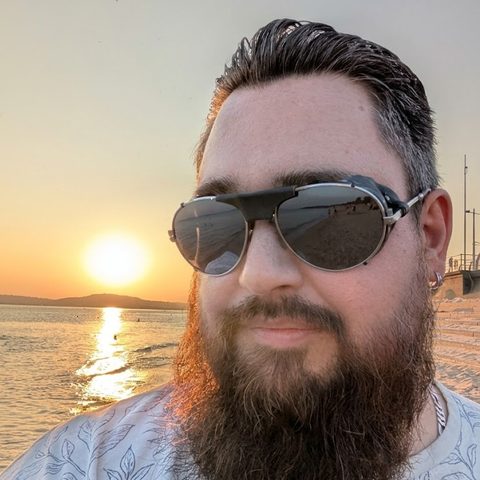 Dayle, smiling in aviator sunglasses on a beach at sunset